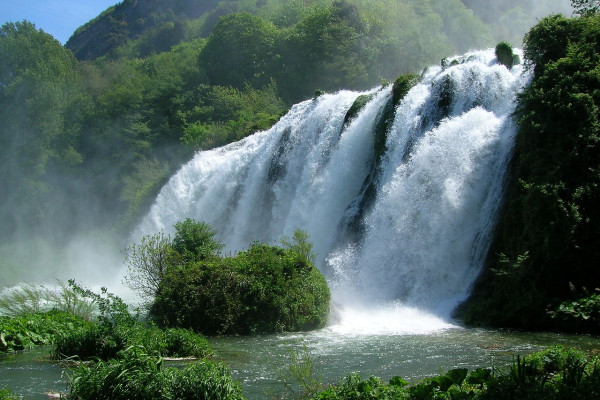 Una cascata situata in un ambiente naturale, circondata da alberi e vegetazione verde.