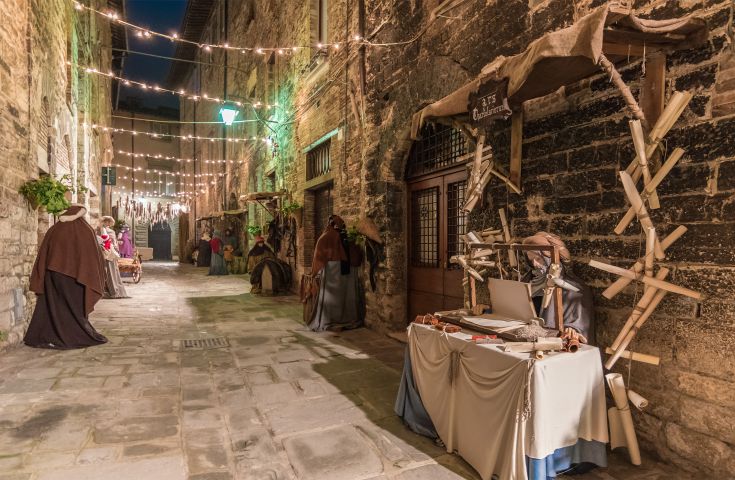 Una scena notturna di un vicolo con mercato medievale, con luci diffuse e figure storiche all'interno di un ambiente tranquillo.