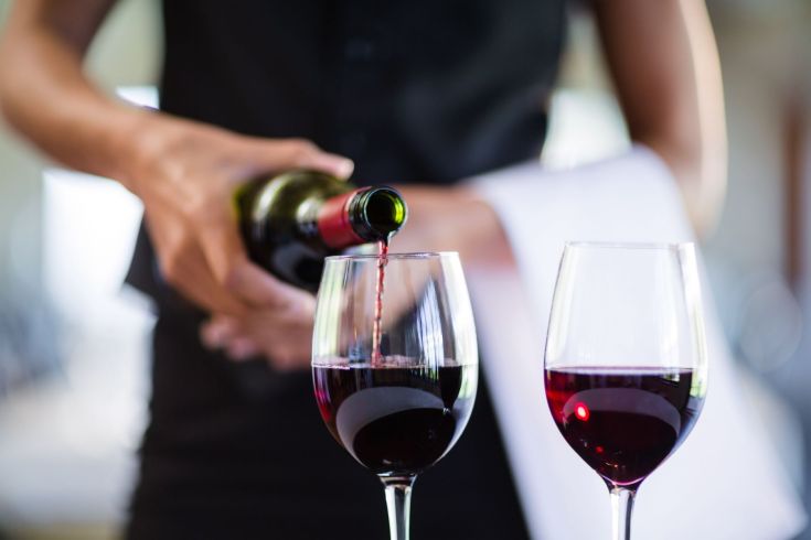 Un cameriere versa del vino rosso in due bicchieri. L'ambiente è tranquillo e accogliente.