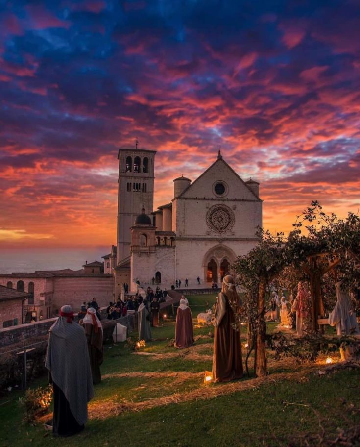 Rappresentazione del presepe con la basilica di Assisi sullo sfondo durante il tramonto.