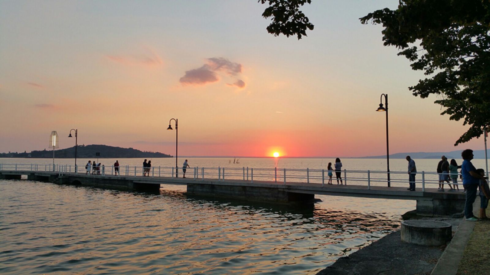 Tramonto su un molo affollato, con sfumature arancioni e rosa nel cielo, creando un'atmosfera tranquilla.