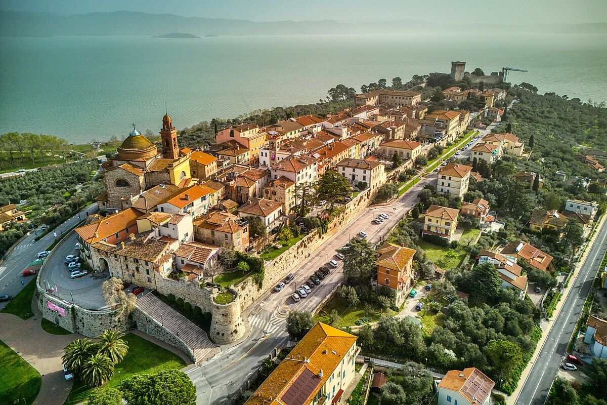 Scena aerea di un borgo caratteristico, immerso nella vegetazione e vicino a un lago.