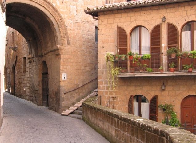 Una tranquilla strada che porta a un antico arco in pietra, circondata da edifici storici.
