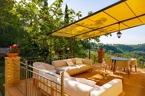 Terrazza all'aperto con divani bianchi e un tavolo, circondata da verdi colline.
