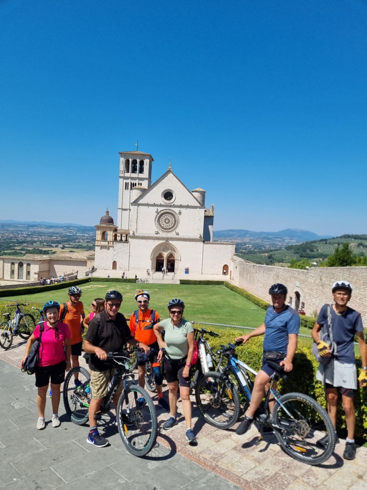 Un gruppo di ciclisti in sosta ad Assisi, immersi nei paesaggi caratteristici e con la basilica sullo sfondo.