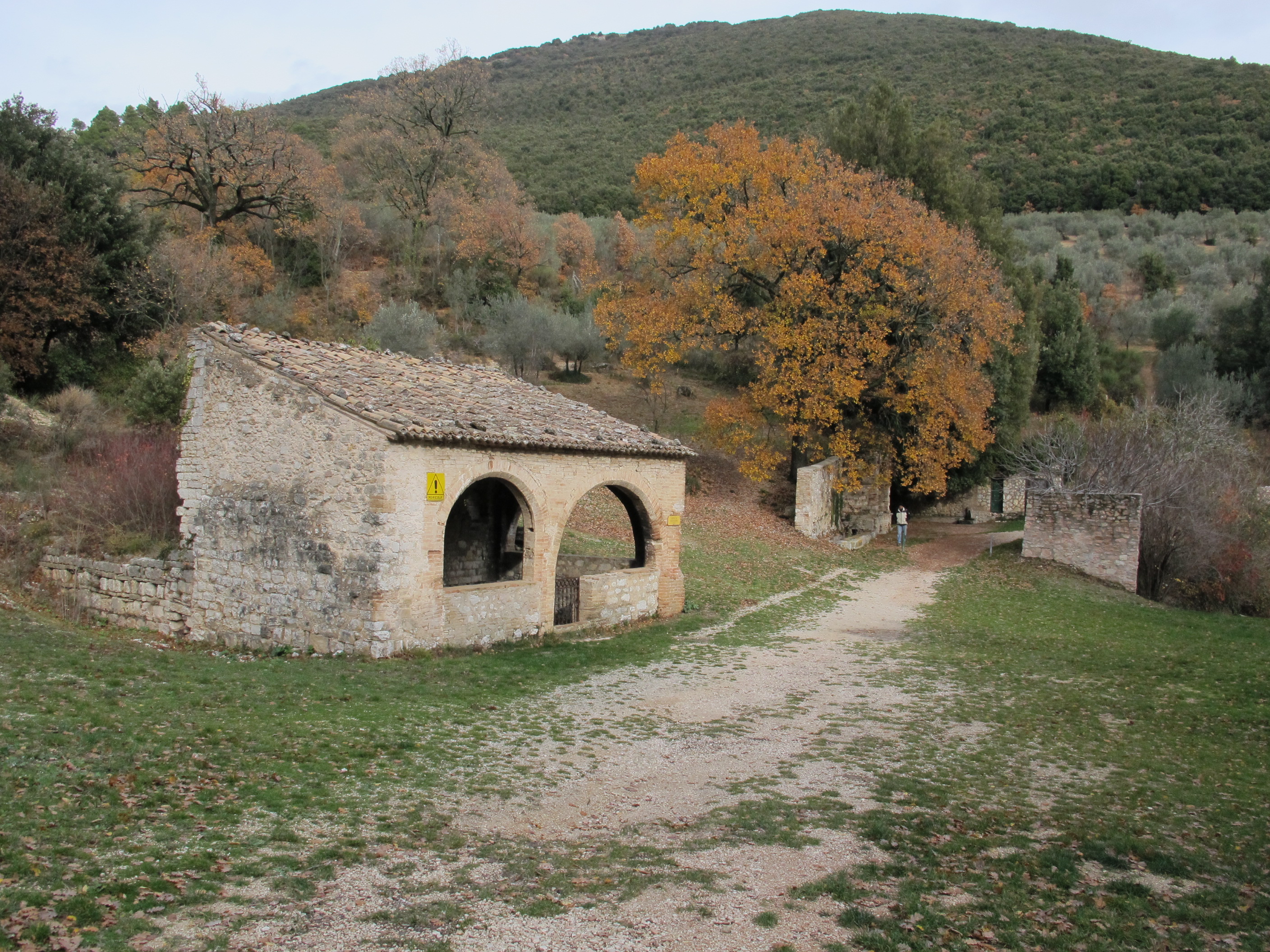 Strada di montagna con  edificio piccolo in pietra e una natura dai colori autunnali.