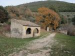 Strada di montagna con edificio piccolo in pietra e una natura dai colori autunnali.