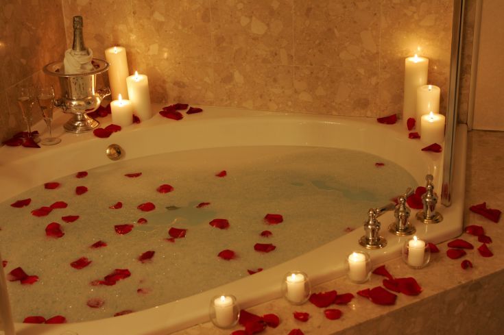 Una vasca da bagno decorata con petali di rosa e candele, creando un'atmosfera accogliente e rilassante.