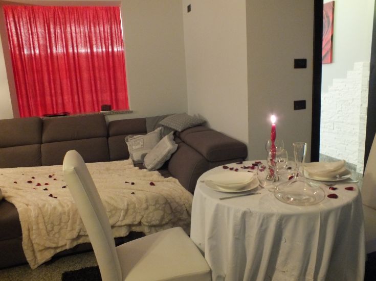 Un angolo accogliente con un tavolo ben apparecchiato per una cena a lume di candela, petali di rosa e un divano comodo.