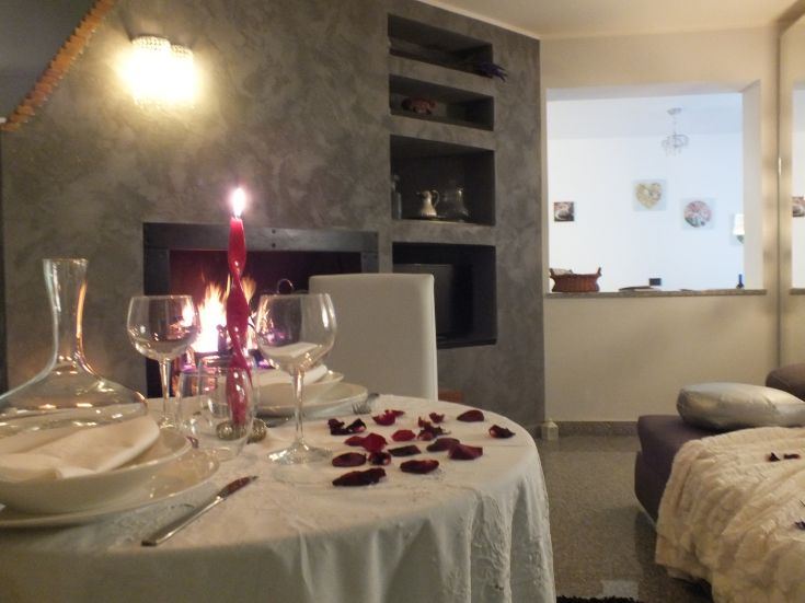 Un tavolo apparecchiato con petali di rosa e una candela accesa, riscaldato da un camino. Ideale per una cena intima.