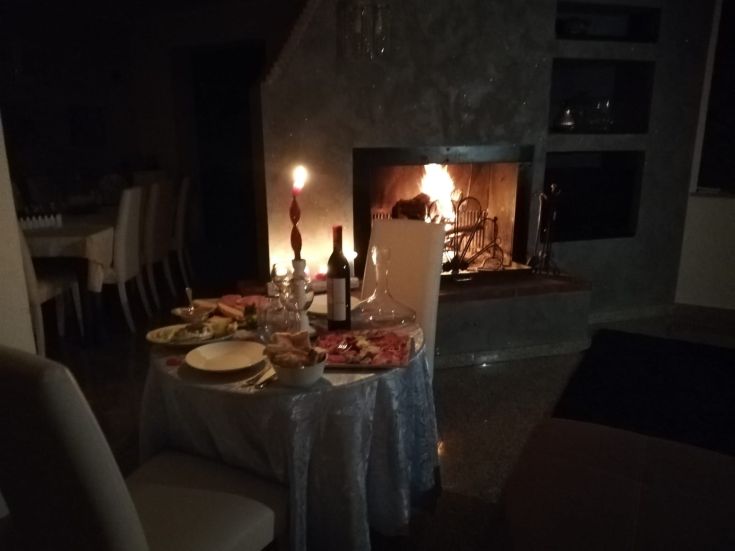 Un tavolo romantico apparecchiato per una cena accogliente, illuminato da candele e con un camino acceso.