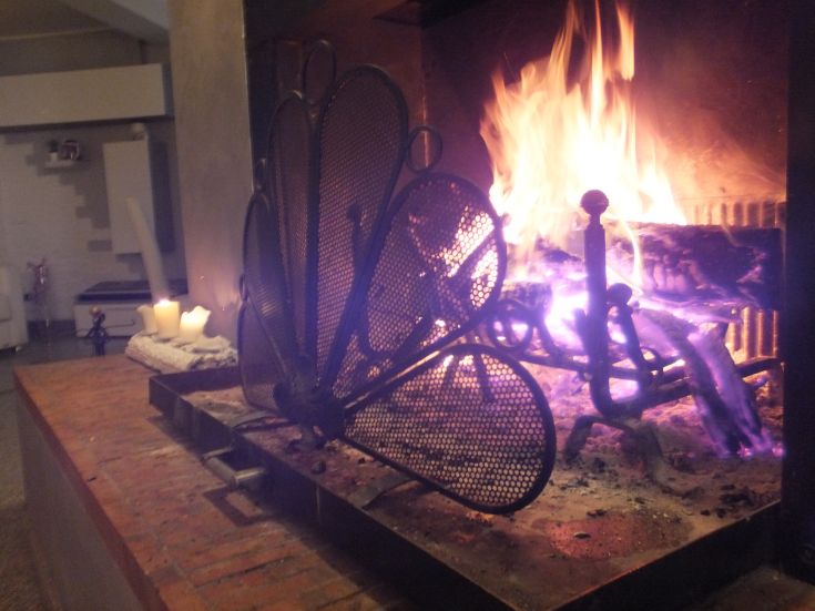 Un camino acceso con fiamme danzanti e candele sullo sfondo, che creano un'atmosfera calda e rilassante.