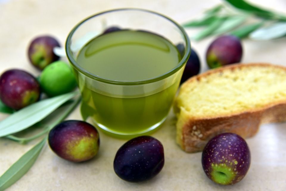 Un bicchiere di olio d'oliva, accompagnato da olive fresche e una fetta di pane.